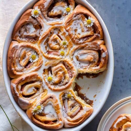 An baking dish of strawberry cinnamon rolls with chamomile and vanilla glaze with one removed.