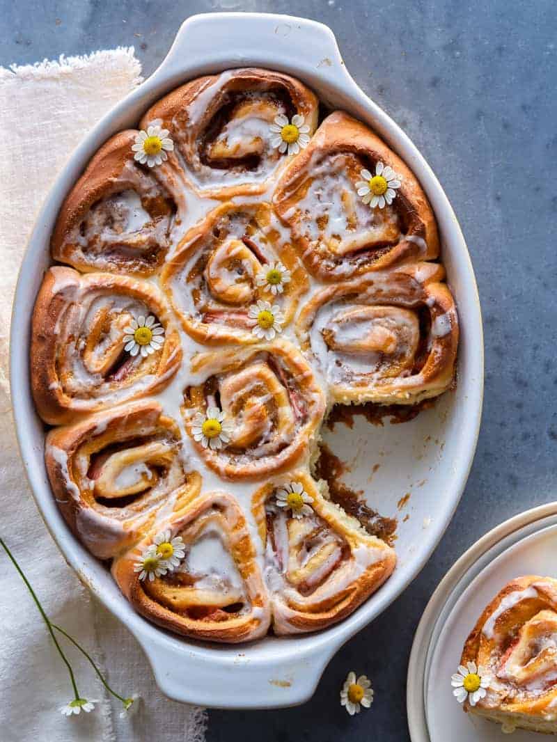 An oval baking dish of strawberry cinnamon rolls with chamomile glaze with one taken out.