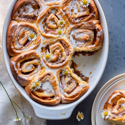 Strawberry cinnamon rolls with a chamomile glaze in a baking dish with one taken out.