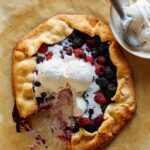 A sliced mixed berry galette with ice cream on the side and on top.