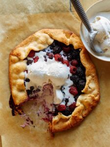 A sliced mixed berry galette with ice cream on the side and on top.