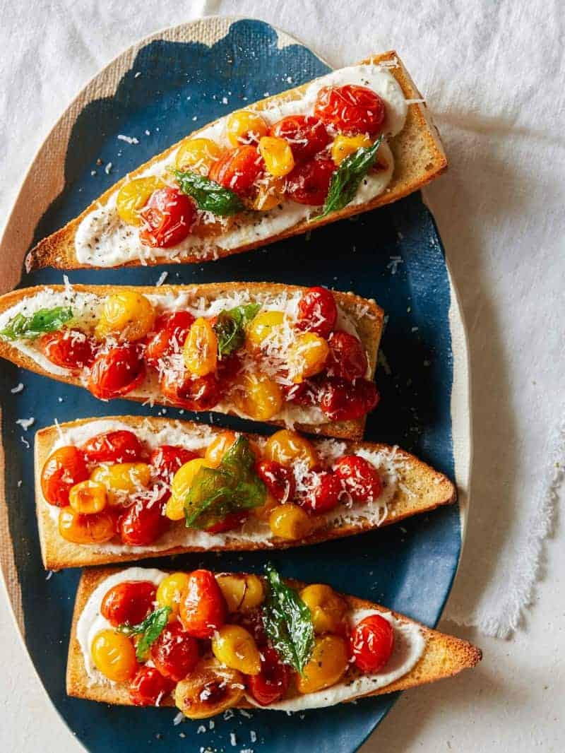 Roasted tomatoes on toasted baguette topped with feta on a platter. 