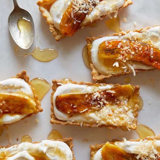 Rectangular banana coconut honey cream tarts with a spoon and honey.