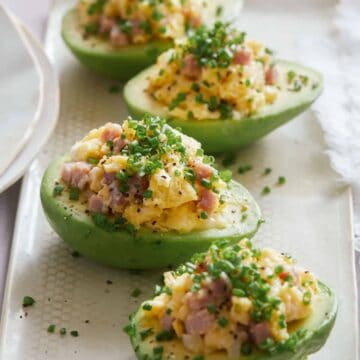 A close up of breakfast scramble stuffed avocados on a white plate.