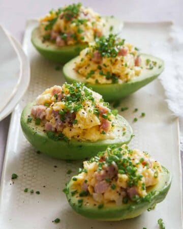 A close up of breakfast scramble stuffed avocados on a white plate.