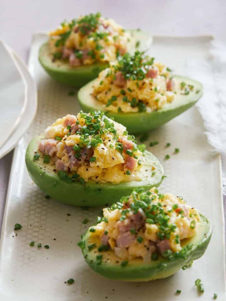 A close up of breakfast scramble stuffed avocados on a white plate.