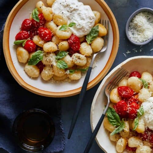 Bowls of caprese gnocchi with cheese, a drink, and forks.