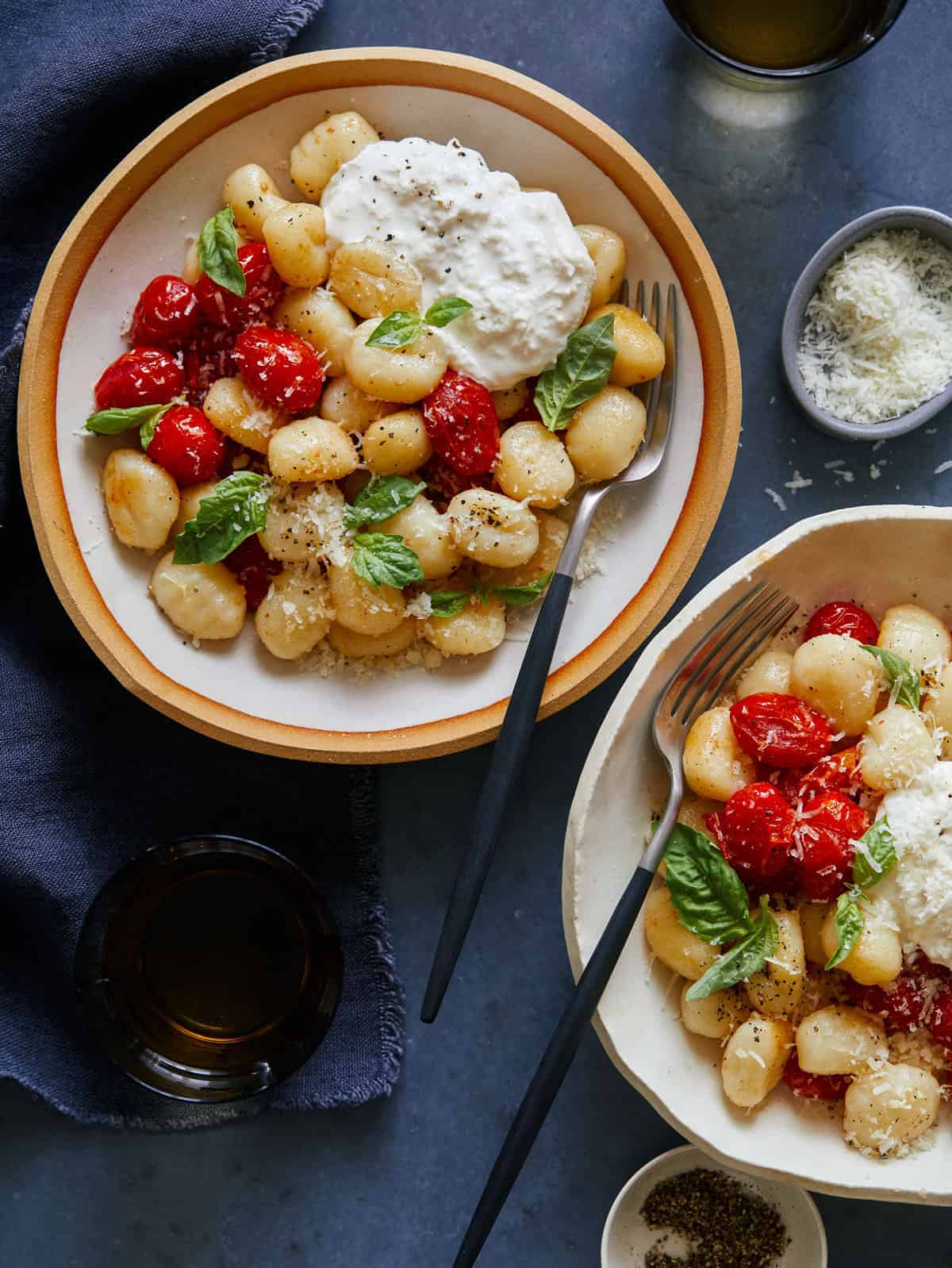 Bowls of caprese gnocchi with cheese, a drink, and forks.