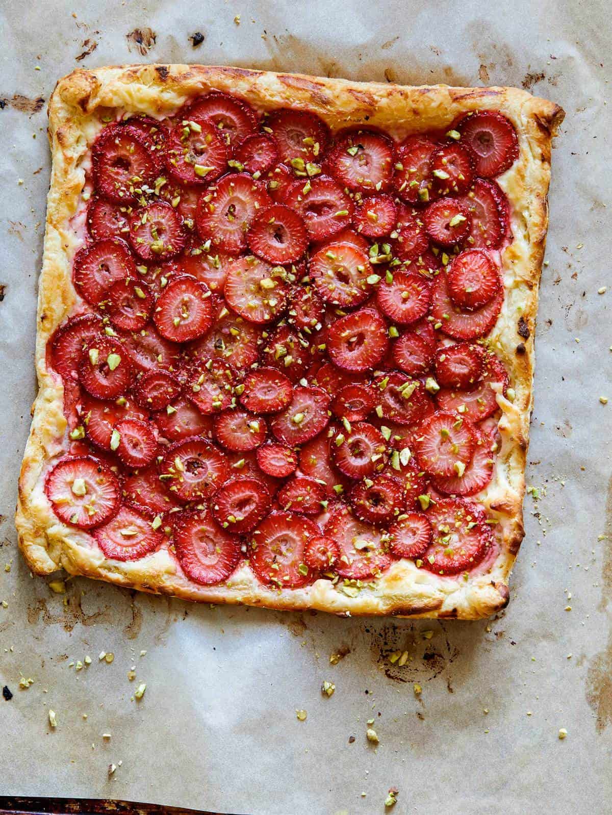 A strawberry tart right out of the oven on a piece of parchment.