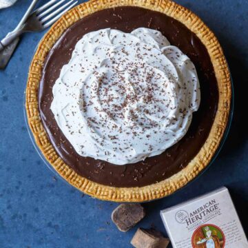 A whole chocolate cream pie with forks and chocolate.