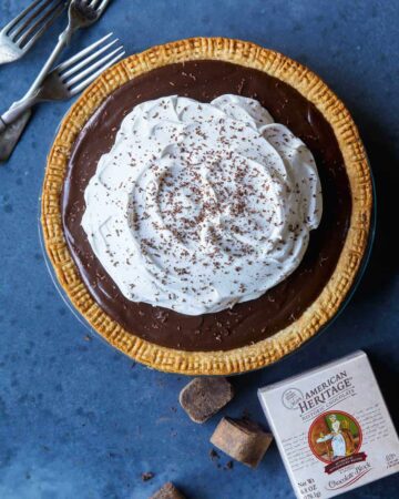 A whole chocolate cream pie with forks and chocolate.