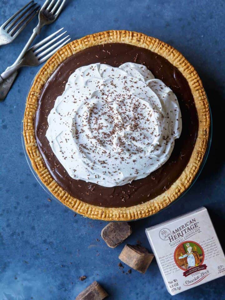 A whole chocolate cream pie with forks and chocolate.