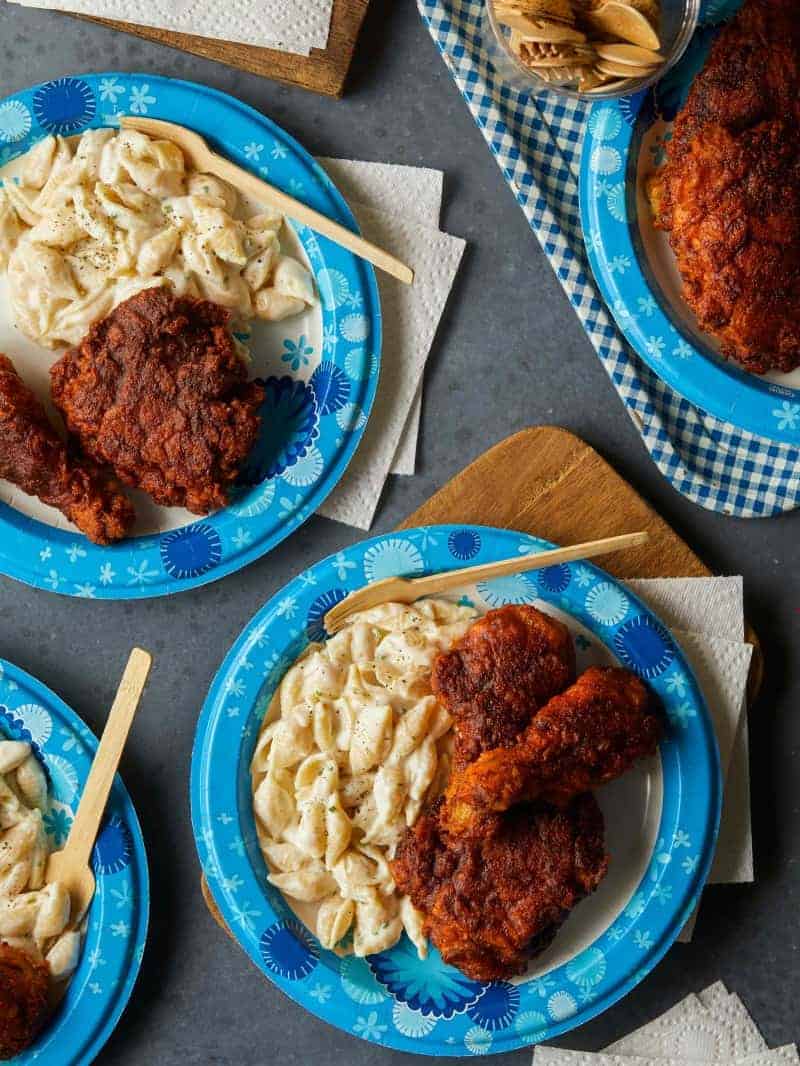 Paper plates of Nashville hot chicken and mac and cheese with wooden forks.