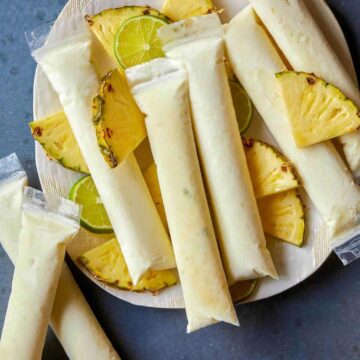A plate of pina colada Italian ice pops with fresh pineapple and lime slices.