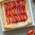 A stone fruit tart on a square plate.