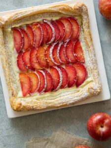 A stone fruit tart on a square plate.