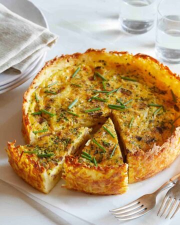 A sliced bacon, cheddar, and chive quiche with hash brown crust.