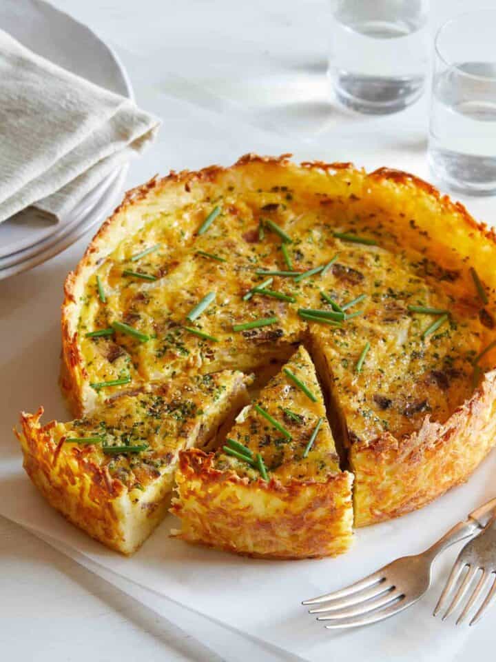 A sliced bacon, cheddar, and chive quiche with hash brown crust.