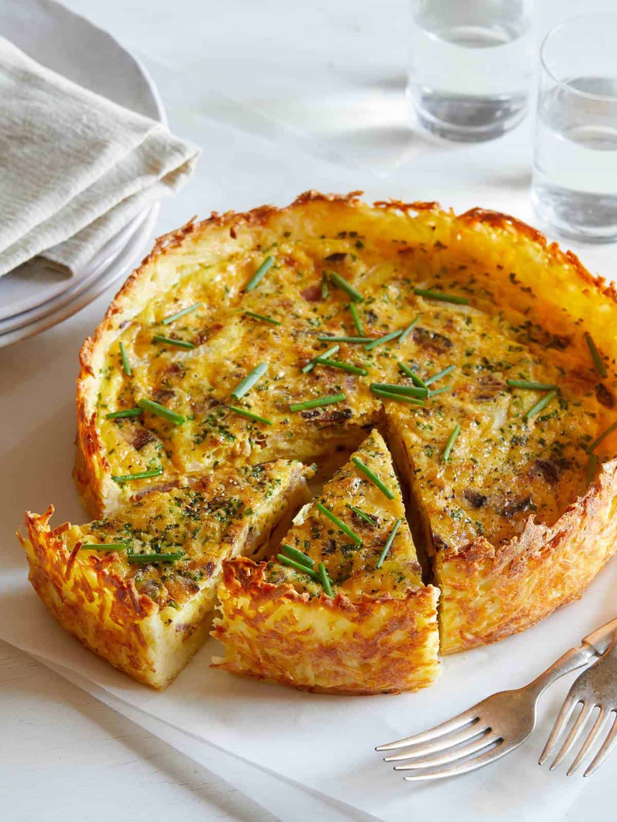 A baon and onion quiche with a hash brown crust on a platter with two slices out. 