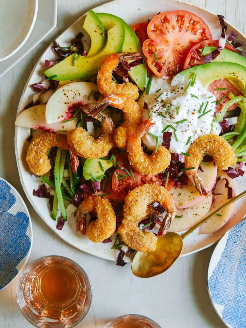 Fried coconut shrimp on top of a bed of lettuce and seasonal summer ingredients.