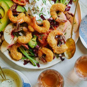 A plate of coconut shrimp summer salad with dressing and drinks on the side.