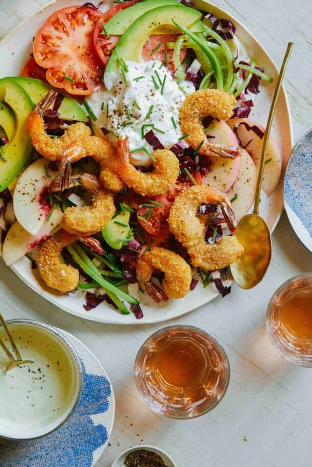 A plate of coconut shrimp summer salad with dressing and drinks on the side.