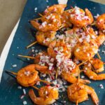 A platter of smoked paprika and garlic shrimp skewers topped with onion.