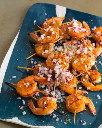 A platter of smoked paprika and garlic shrimp skewers topped with onion.