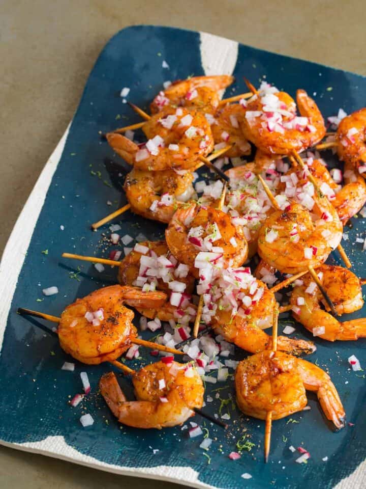 A platter of smoked paprika and garlic shrimp skewers topped with onion.