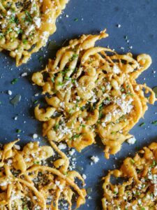 A close up of savory funnel cakes finished with honey, cheese, chives, and sea salt.