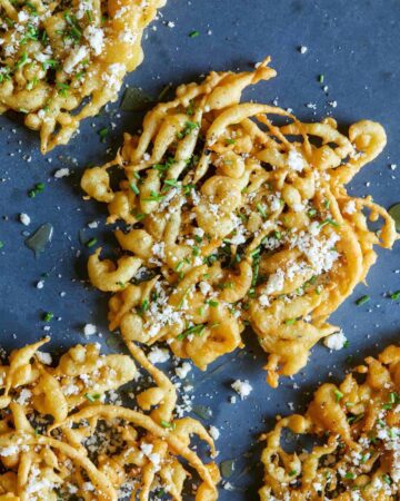 A close up of savory funnel cakes finished with honey, cheese, chives, and sea salt.