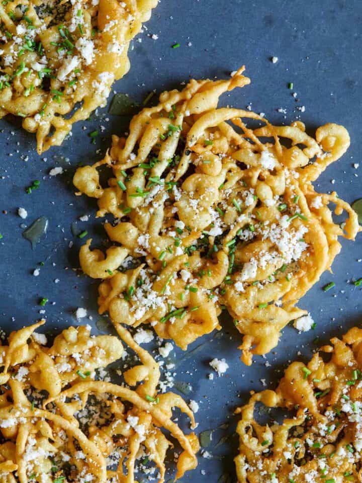 A close up of savory funnel cakes finished with honey, cheese, chives, and sea salt.