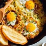 Simple cheesy skillet hash browns and eggs with bread and a wooden spoon.