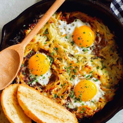 Simple cheesy skillet hash browns and eggs with bread and a wooden spoon.