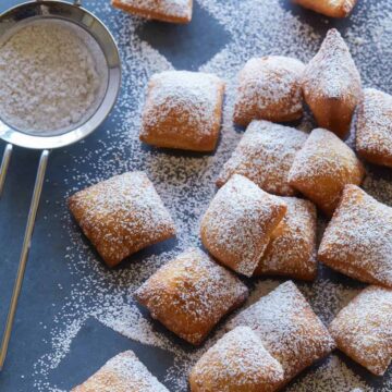 Chai spiced buttermilk beignets covered in powdered sugar with a small sieve.