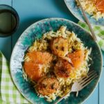 Plates of browned butter seared scallops over lemon orzo with forks and a drink.