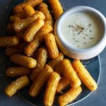 A plate of savory herb churros with white queso dip on the side.