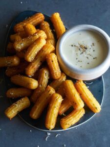 A plate of savory herb churros with white queso dip on the side.