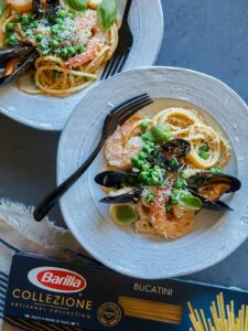 A plate of seafood carbonara with a fork and a box of Barilla Collezione Bucatini.