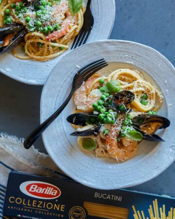 A plate of seafood carbonara with a fork and a box of Barilla Collezione Bucatini.