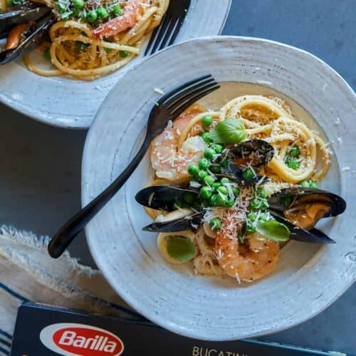 A plate of seafood carbonara with a fork and a box of Barilla Collezione Bucatini.