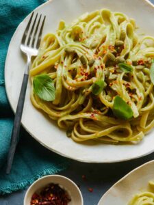 A close up of fettuccine with creamy avocado garlic sauce in a bowl with a fork.