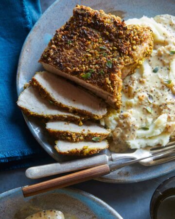 A close up of sliced pistachio crusted pork chop with mashed potatoes, a fork and knife.