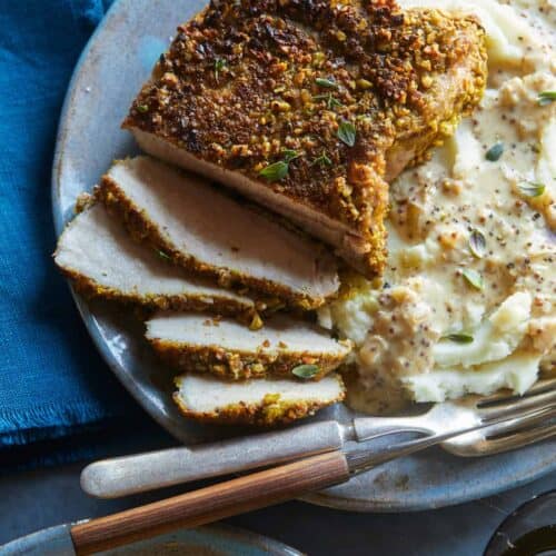 A close up of sliced pistachio crusted pork chop with mashed potatoes, a fork and knife.