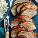 A platter of sliced char siu pork tenderloin next to white rice and a carving fork.