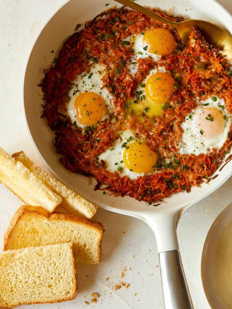 Cheesy Sweet Potatoes Hash Browns in a skillet with fried eggs. 