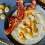 A bowl of creamy vegan cauliflower chowder with crackers and bacon.