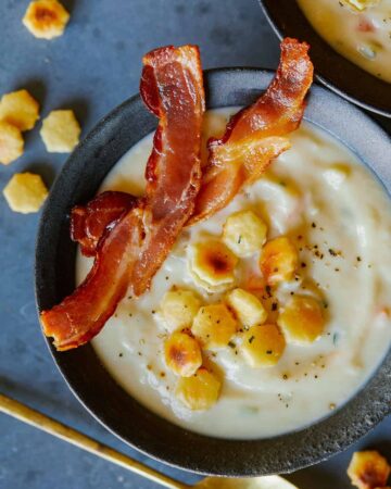 A bowl of creamy vegan cauliflower chowder with crackers and bacon.
