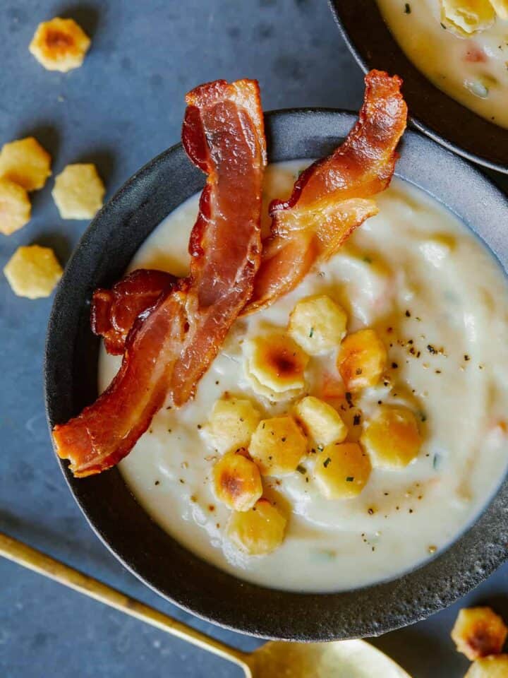 A bowl of creamy vegan cauliflower chowder with crackers and bacon.