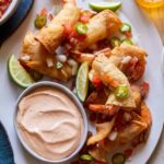 A platter of shrimp taquitos with lime wedges and creamy chipotle sauce on the side.